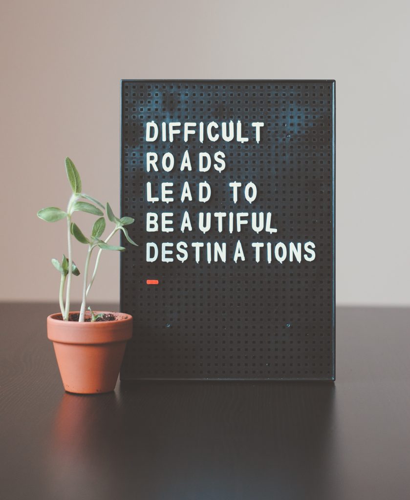 Skylt med texten “Difficult roads lead to beautiful destinations” bredvid en liten krukväxt